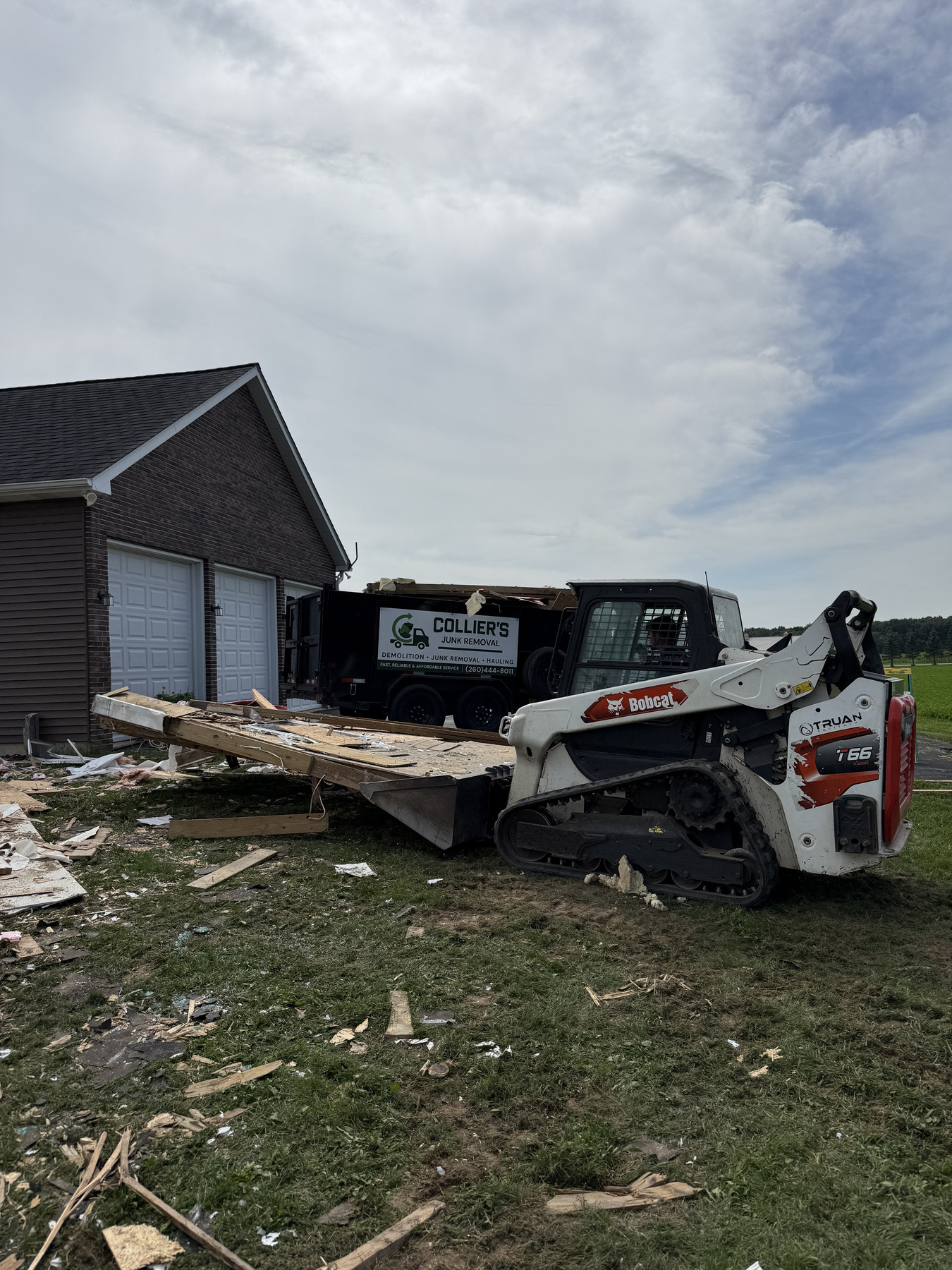Collier's dump truck and Bobcat track loader parked at a demolition job beside a garage